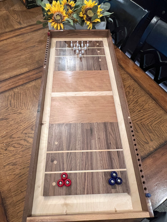 Wooden shuffleboard table with three red and one blue shuffleboard disc on a wooden floor.