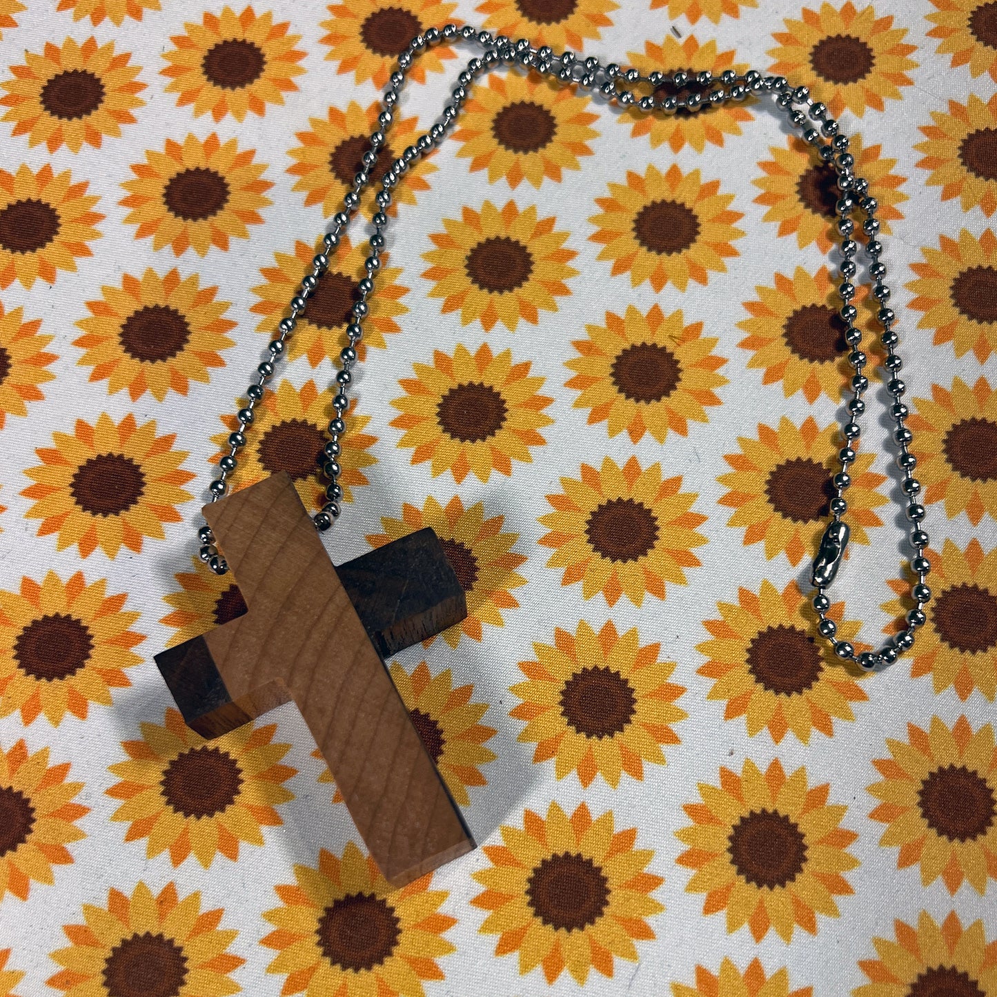 Wooden cross pendant on a chain against a sunflower patterned background