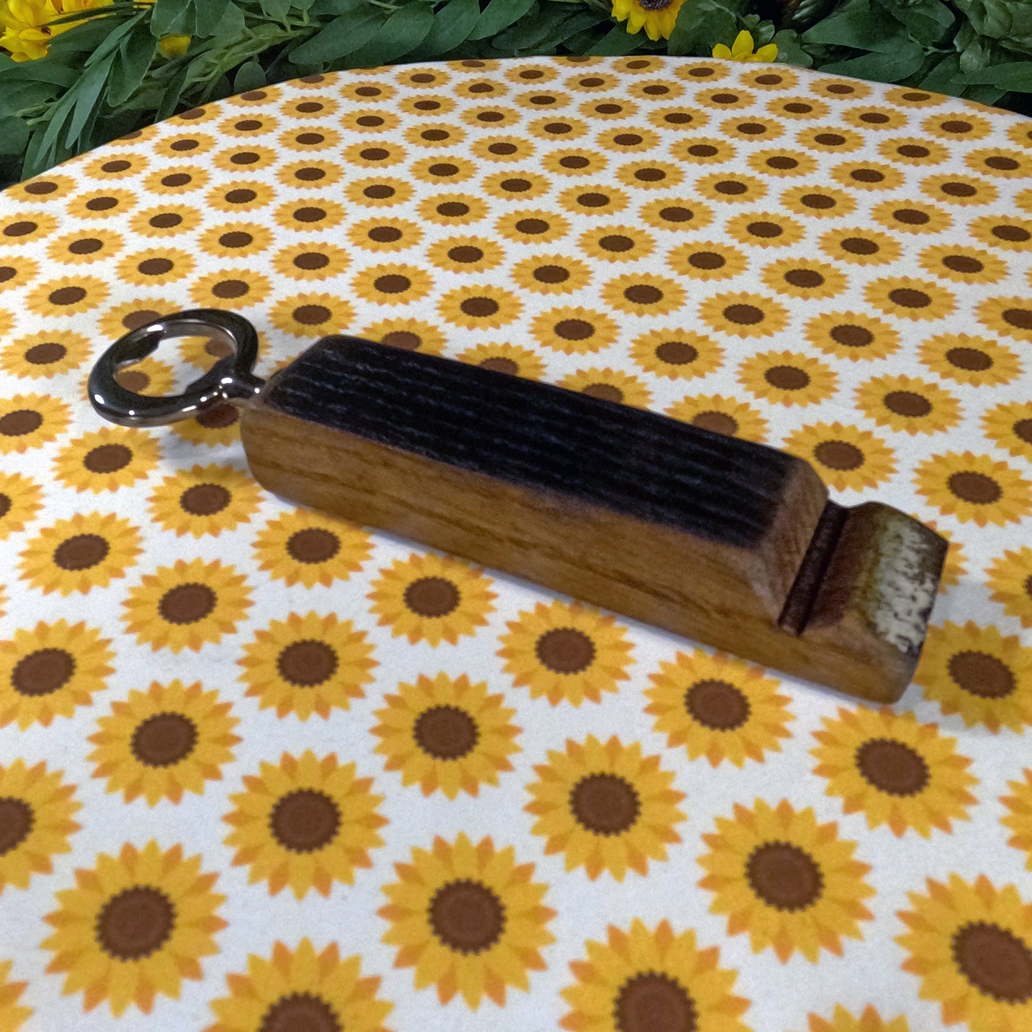 Wooden bottle opener with a black handle on a sunflower-patterned fabric