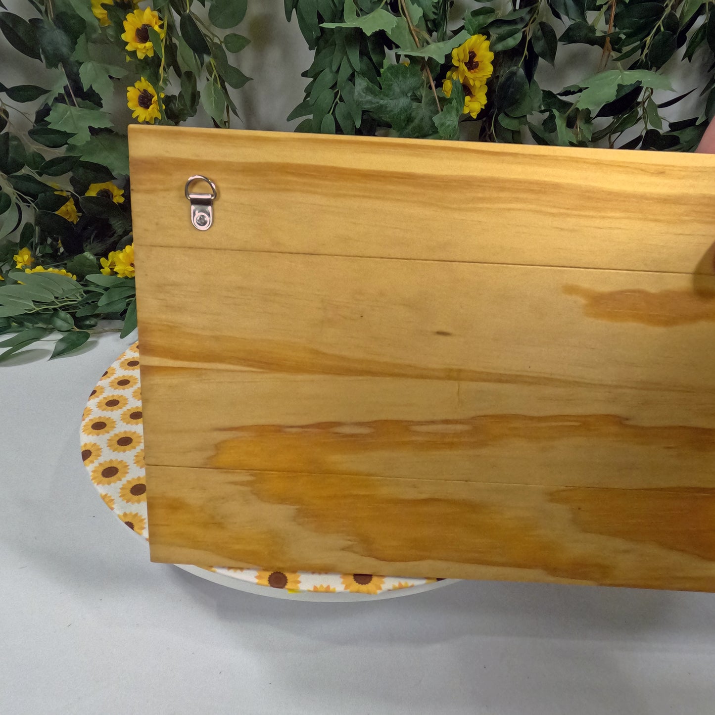Wooden plaque with floral pattern on a white surface with greenery and yellow flowers in the background