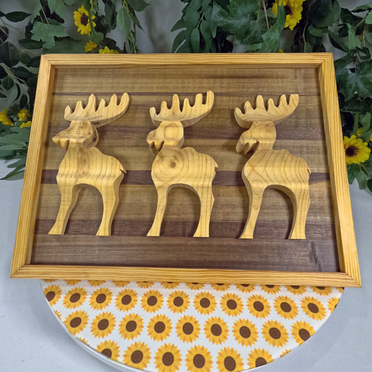 Wooden moose figurines on a wooden frame with a floral-patterned tablecloth underneath.