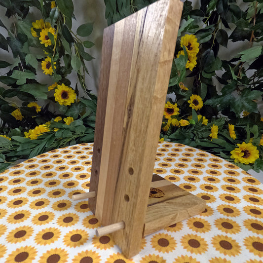Wooden phone stand on a tablecloth with sunflower pattern, surrounded by greenery and sunflowers.