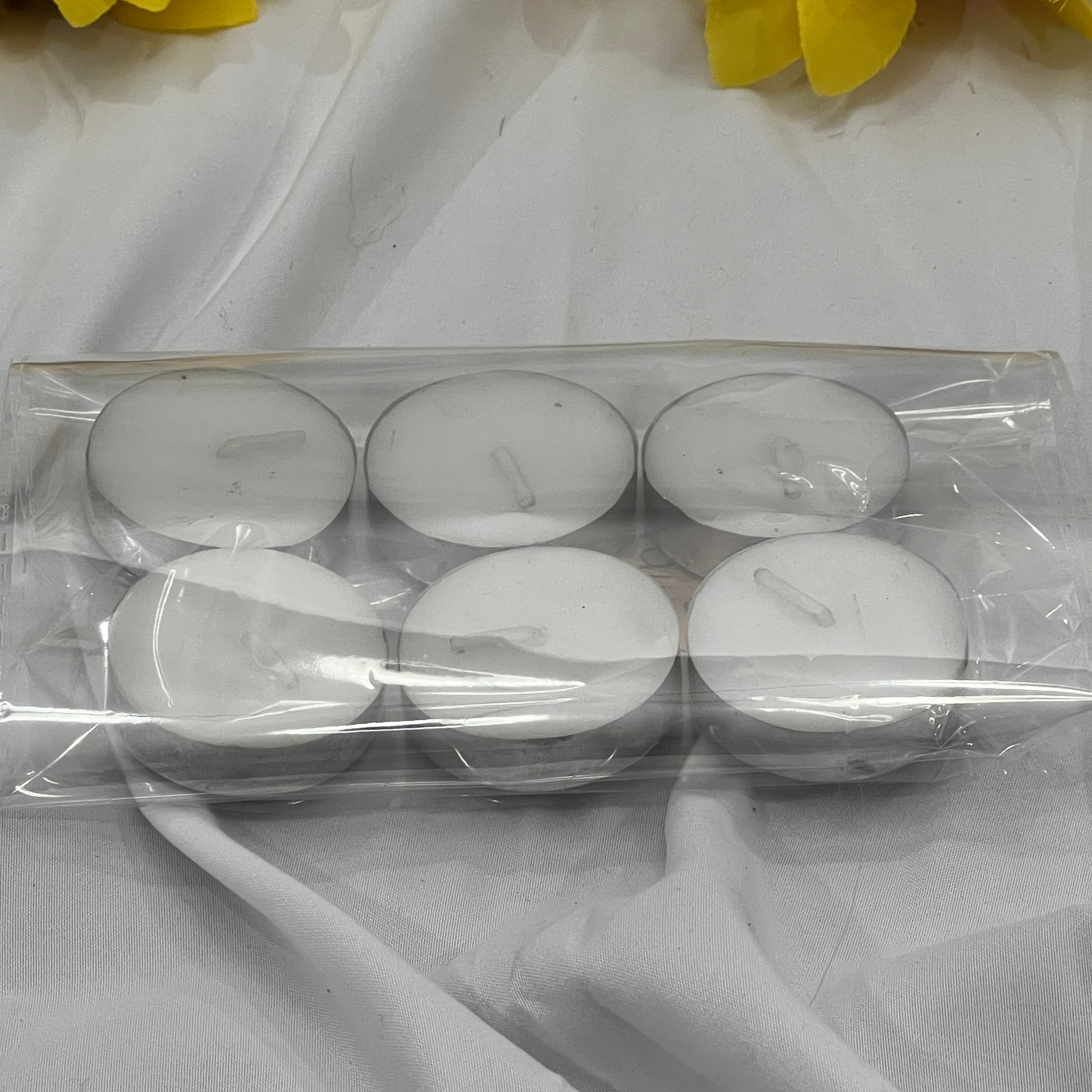 Set of six white tea light candles in clear packaging on a white fabric background