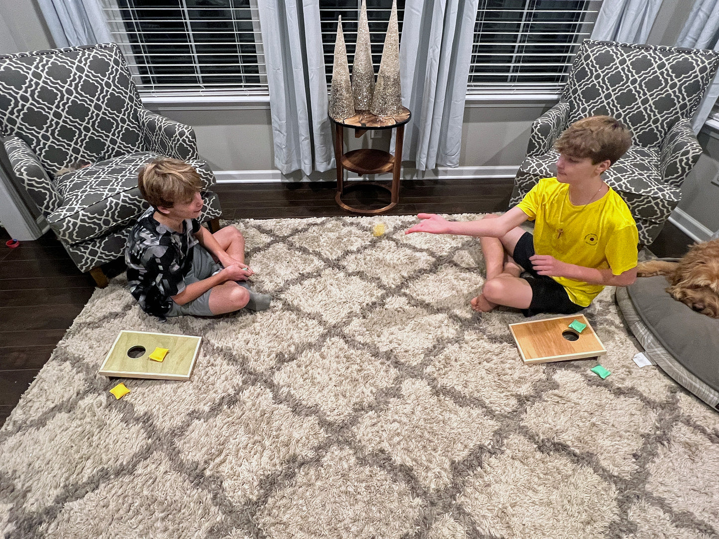 Two children playing cornhole on a carpeted floor in a living room.