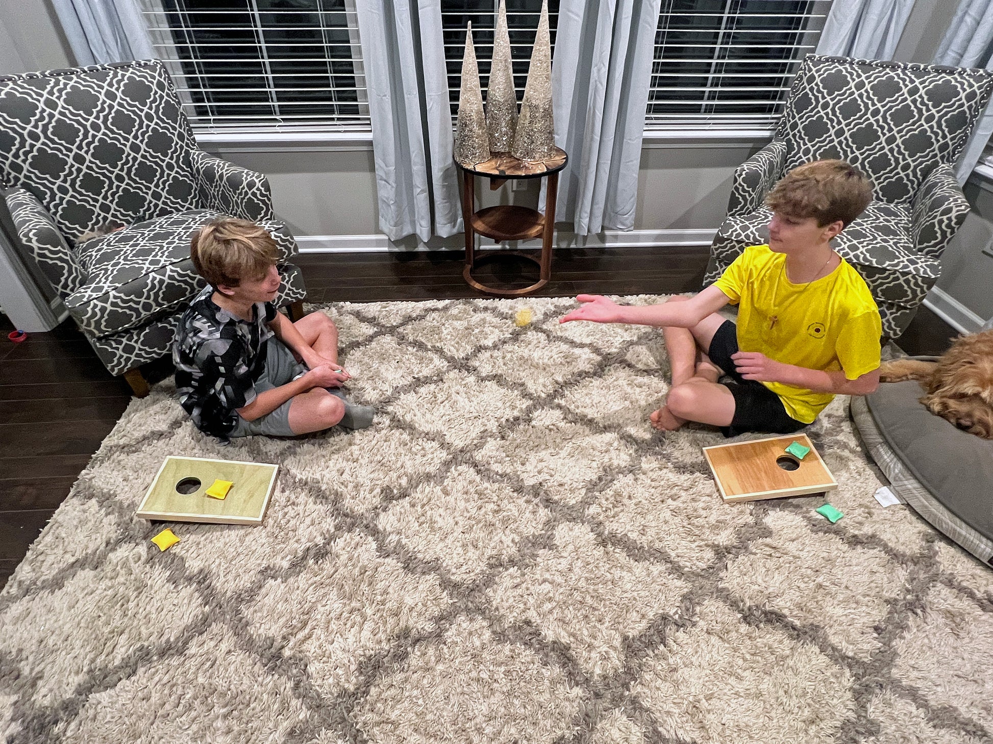 Two children playing cornhole on a carpeted floor in a living room.