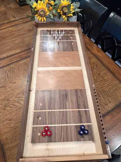 Wooden shuffleboard table with three red and one blue shuffleboard disc on a wooden floor.