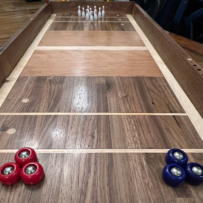 Wooden shuffleboard table with red and blue pucks and white bottles at the end.