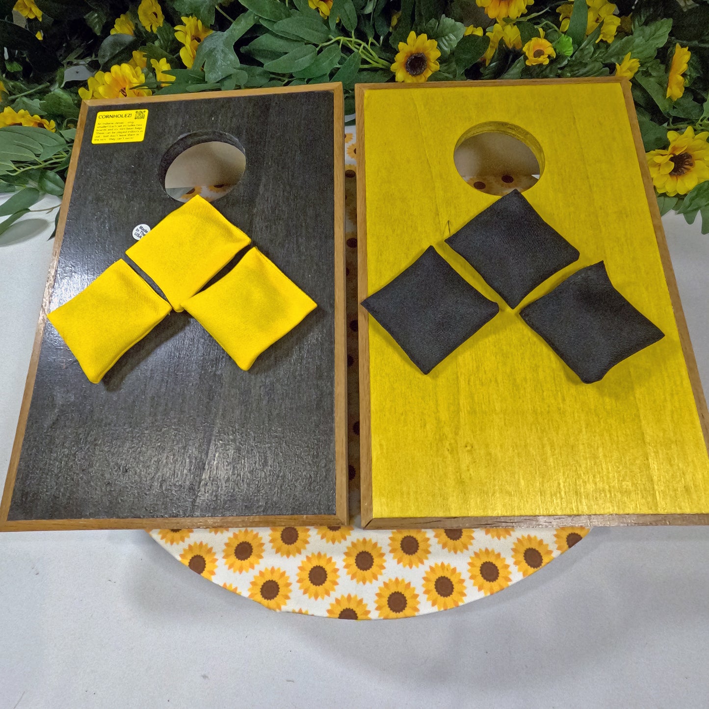 Two wooden cornhole boards with yellow and black bags on a floral-patterned surface.