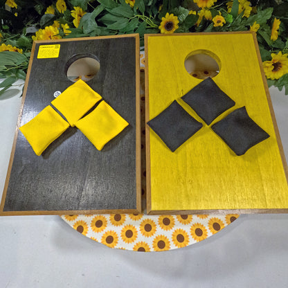 Two wooden cornhole boards with yellow and black bags on a floral-patterned surface.