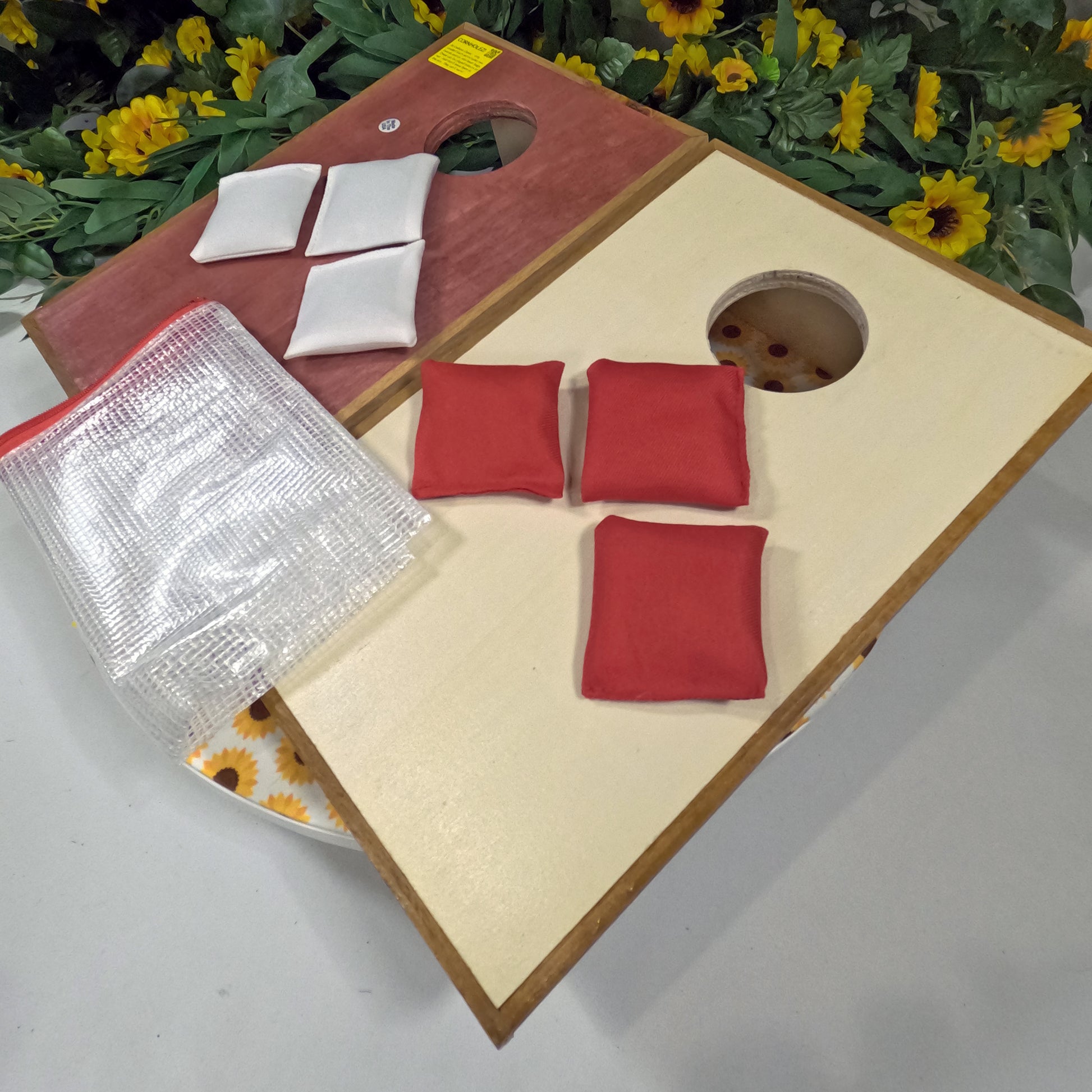 Cornhole board with red and white bags on a table with flowers in the background
