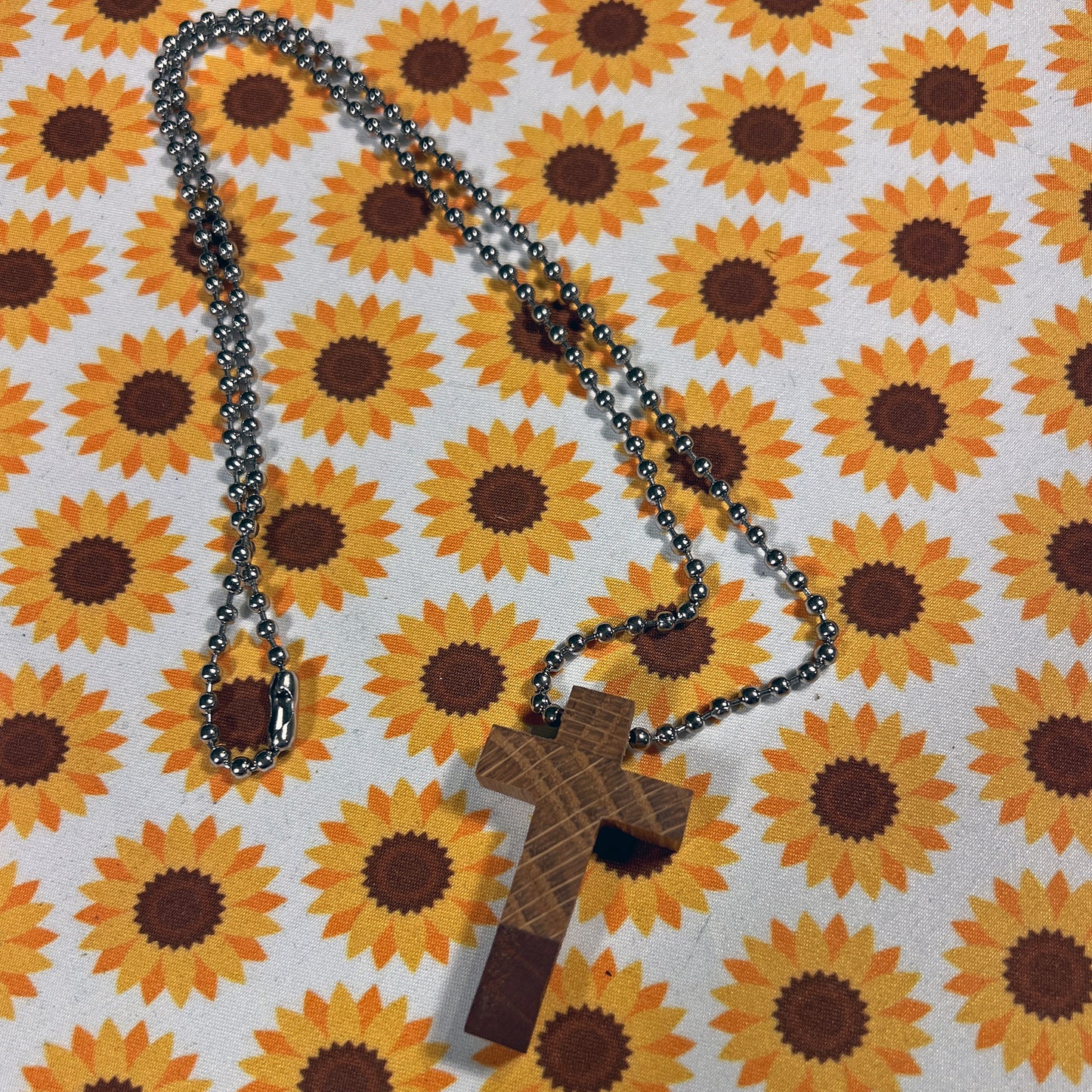 Wooden cross pendant on a chain against a sunflower patterned background