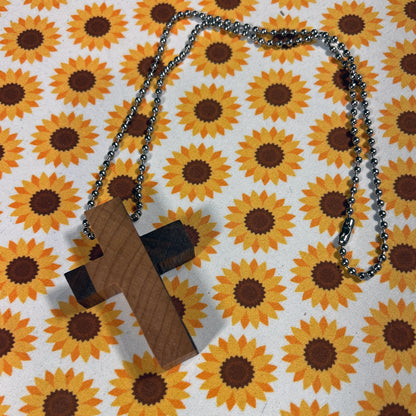 Wooden cross pendant on a chain against a sunflower patterned background