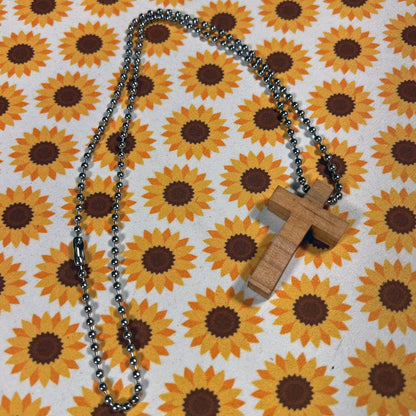 Wooden cross pendant on a chain against a sunflower patterned background