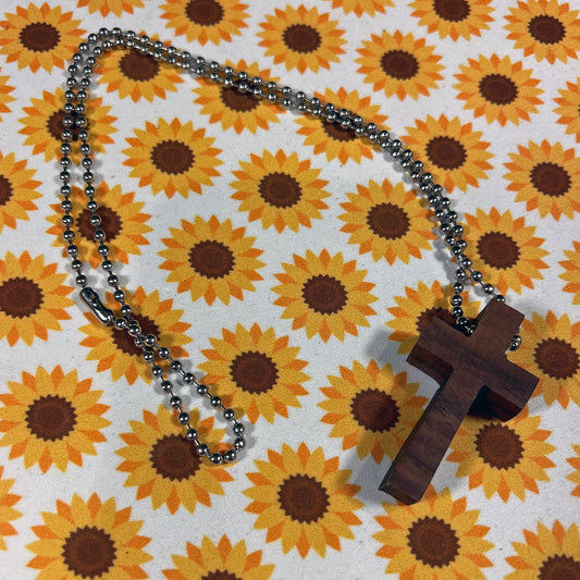 Wooden cross pendant on a chain against a sunflower patterned background