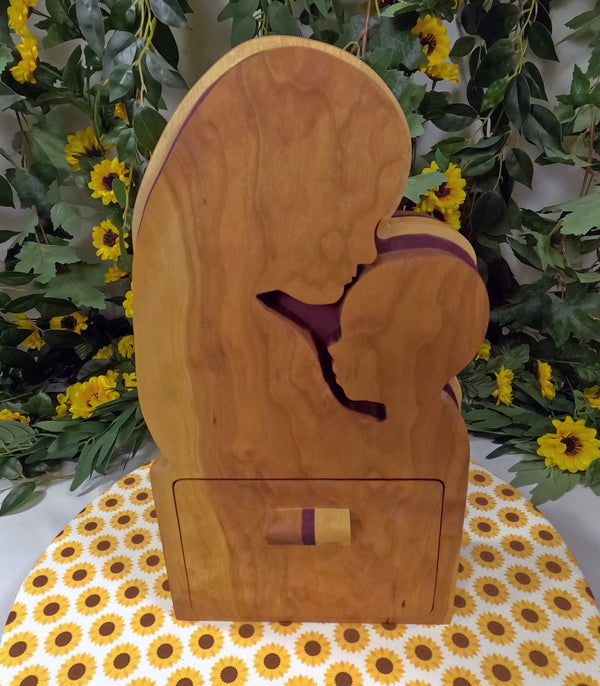 Wooden box with a cutout design of a person in a purple garment, placed on a floral-patterned surface with greenery and flowers in the background.