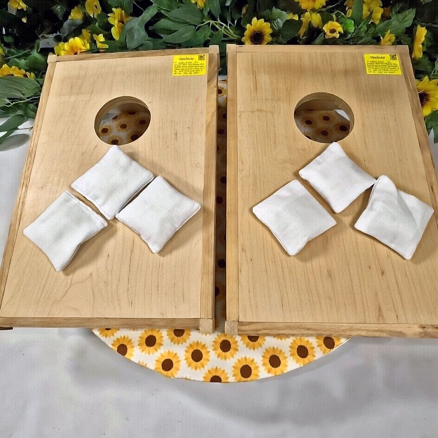 Two wooden cornhole boards with white bags on a table with sunflower patterned cloth.