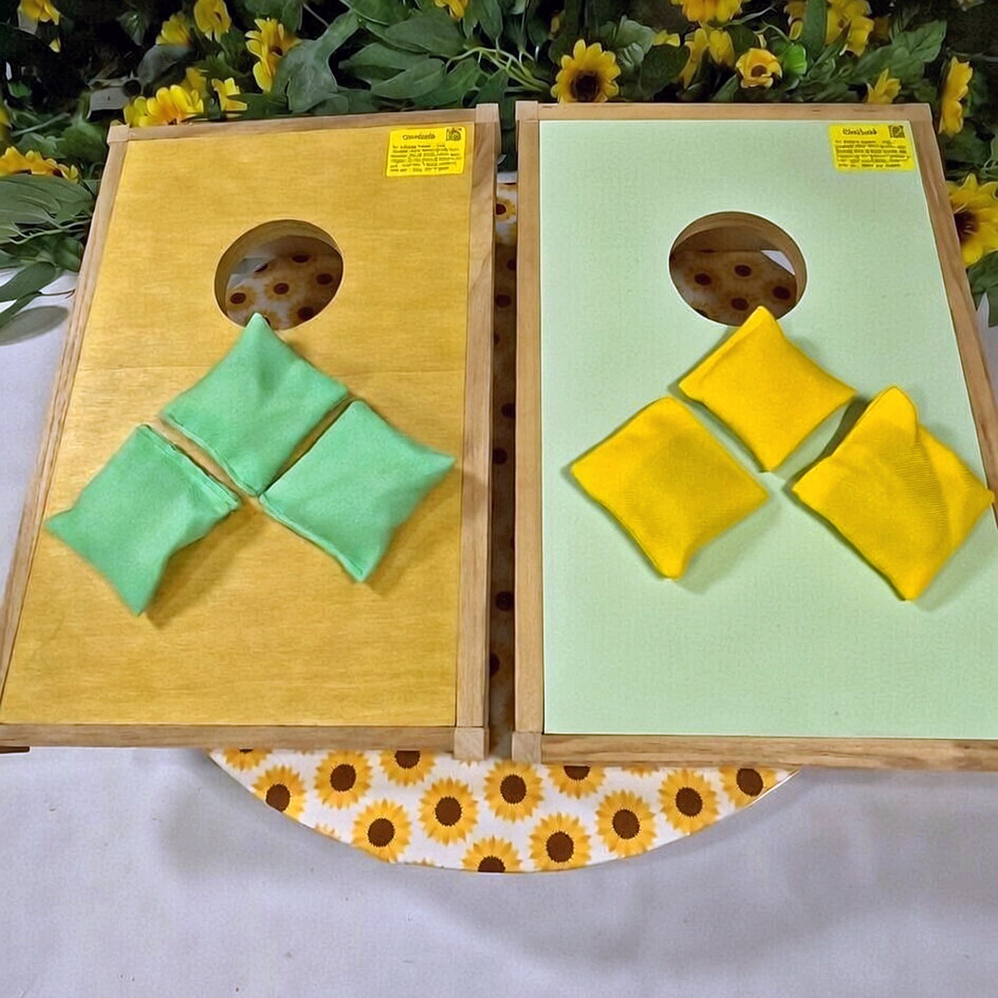 Two cornhole boards with green and yellow bags on a floral-patterned surface.