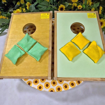 Two cornhole boards with green and yellow bags on a floral-patterned surface.