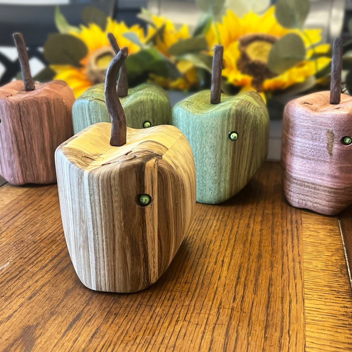 Wooden apple-shaped figurines with stem and leaf accents on a wooden surface.