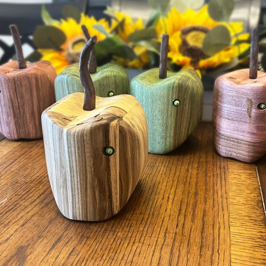 Wooden apple-shaped figurines with stem and leaf accents on a wooden surface.