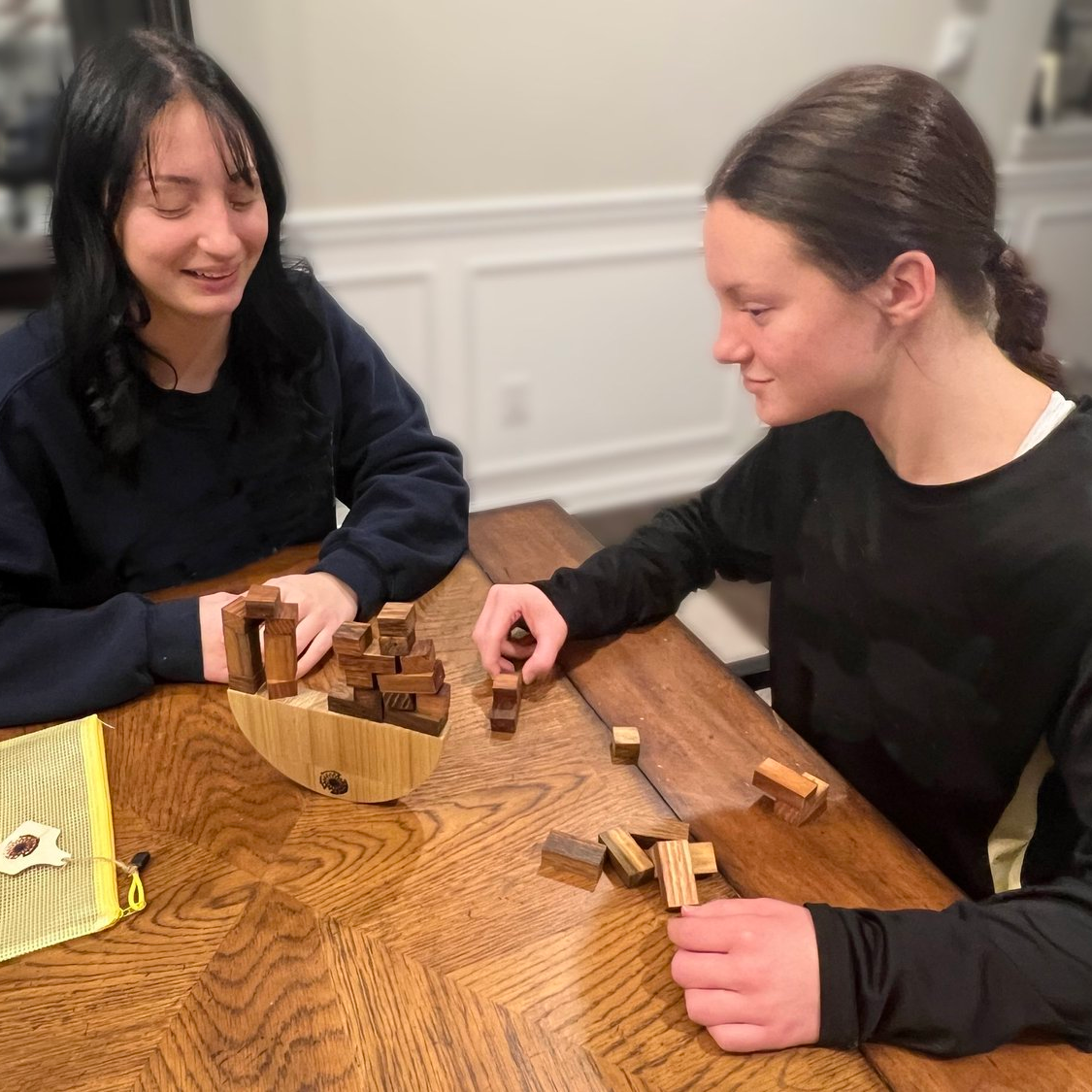 Two people playing with a wooden puzzle on a wooden table.