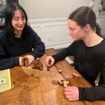 Two people playing with a wooden puzzle on a wooden table.
