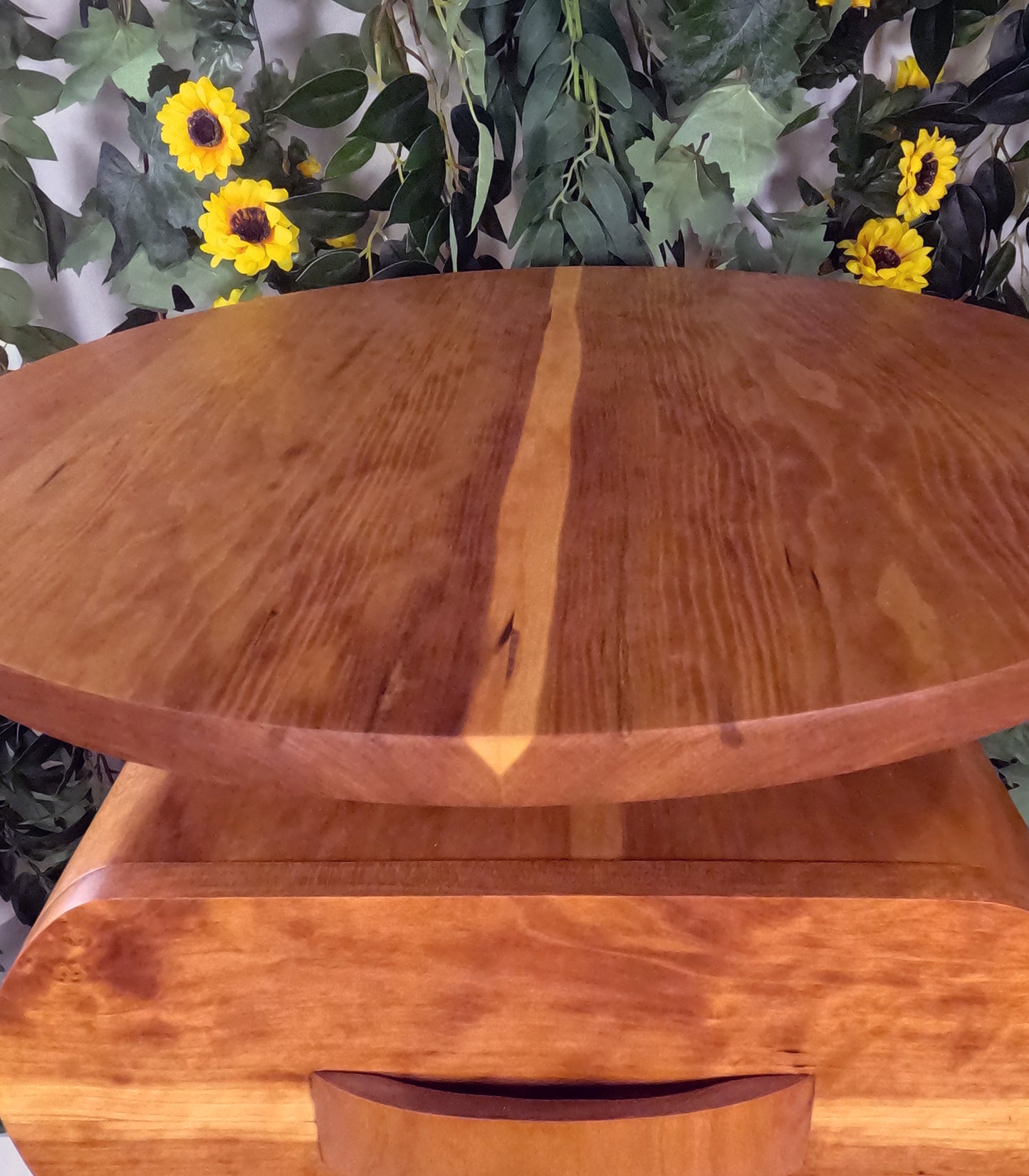 Wooden table with a natural finish in front of green foliage and yellow flowers