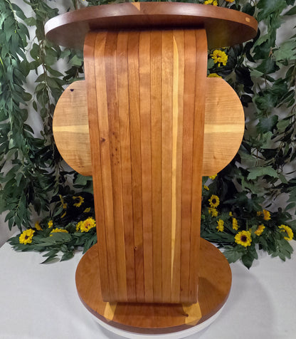 Wooden pedestal with a circular design against a decorative background with greenery and yellow flowers.