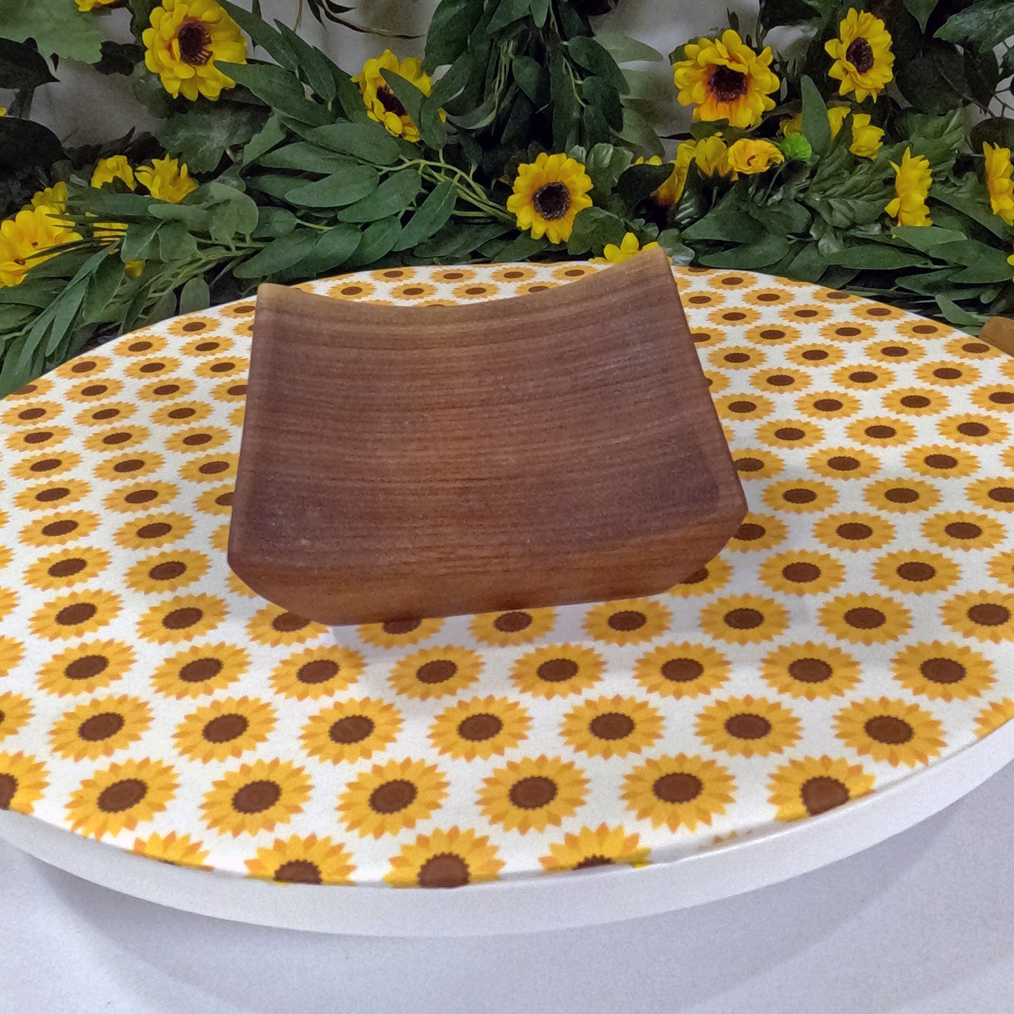 Wooden tray on a tablecloth with sunflower pattern, surrounded by sunflowers and greenery.
