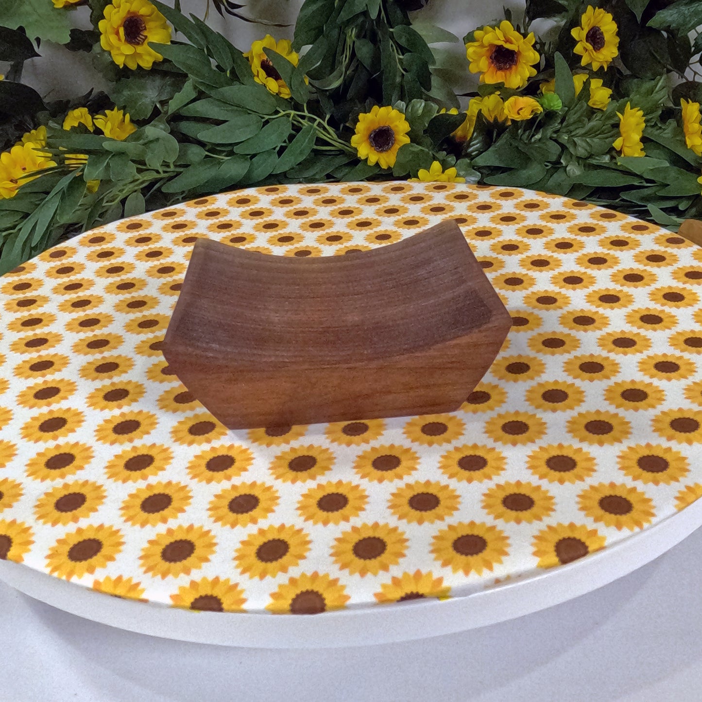 Wooden tray on a tablecloth with sunflower pattern, surrounded by sunflowers and greenery.