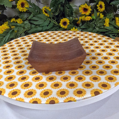 Wooden tray on a tablecloth with sunflower pattern, surrounded by sunflowers and greenery.