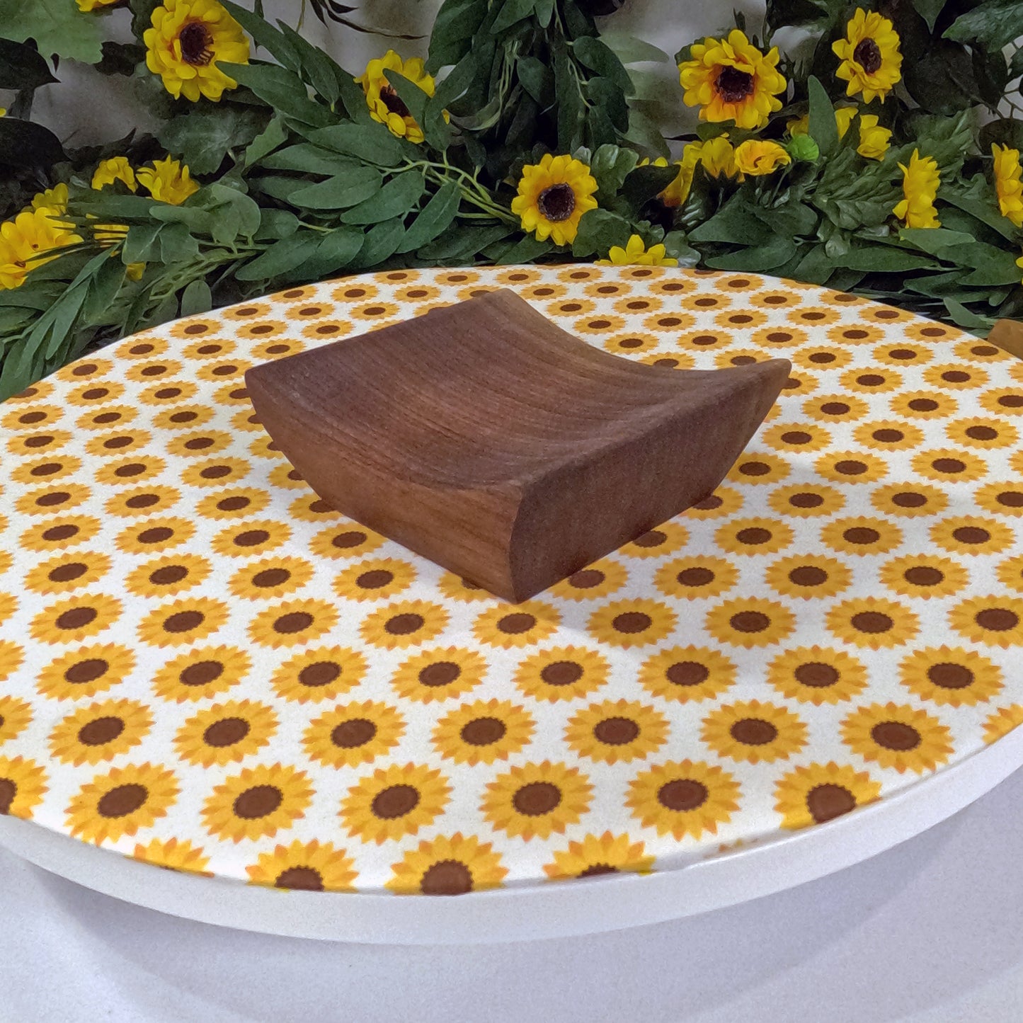 Wooden tray on a tablecloth with sunflower pattern, surrounded by sunflowers and greenery.