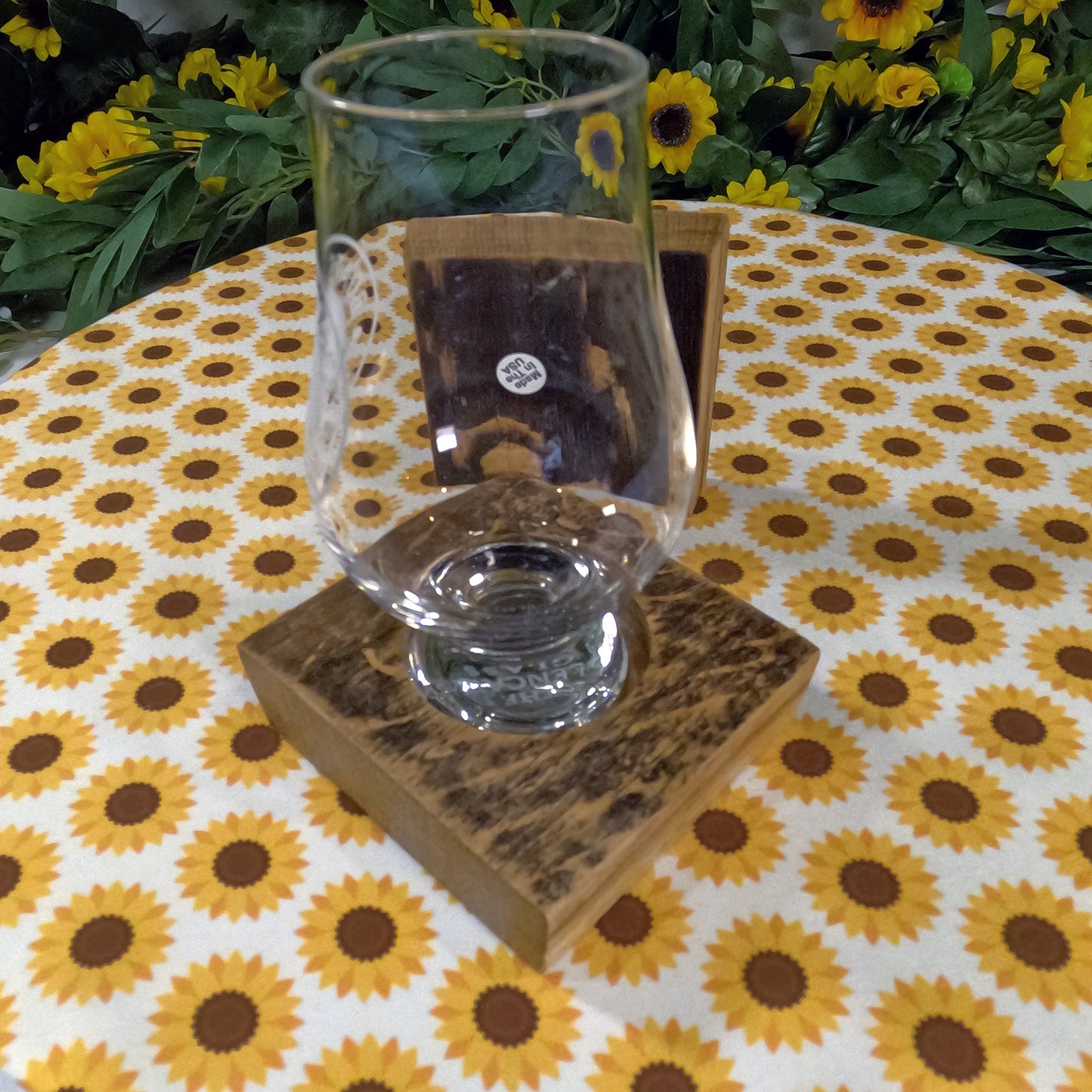 Clear glass on a wooden coaster with a sunflower-patterned tablecloth