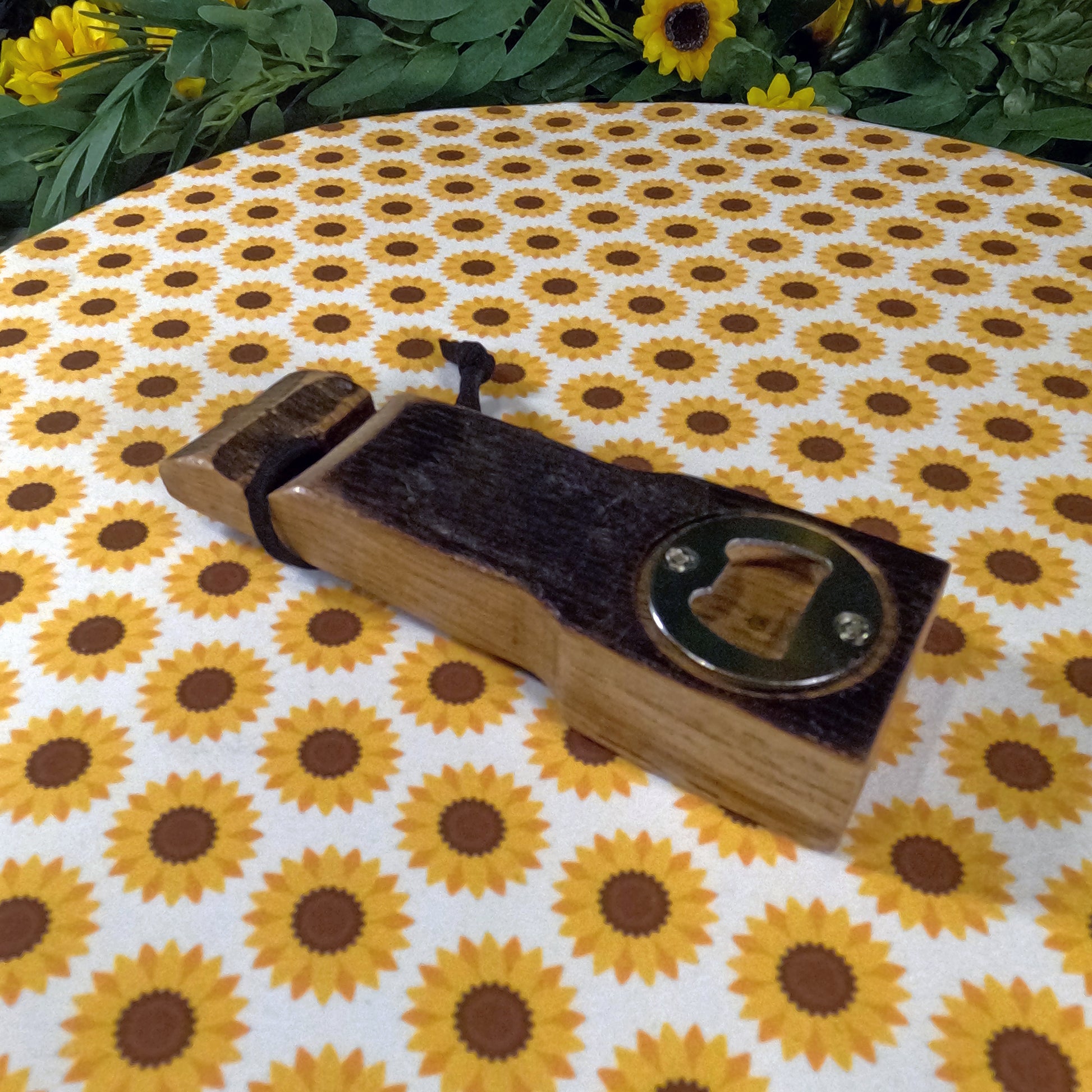 Wooden bottle opener with leather strap on a sunflower-patterned fabric
