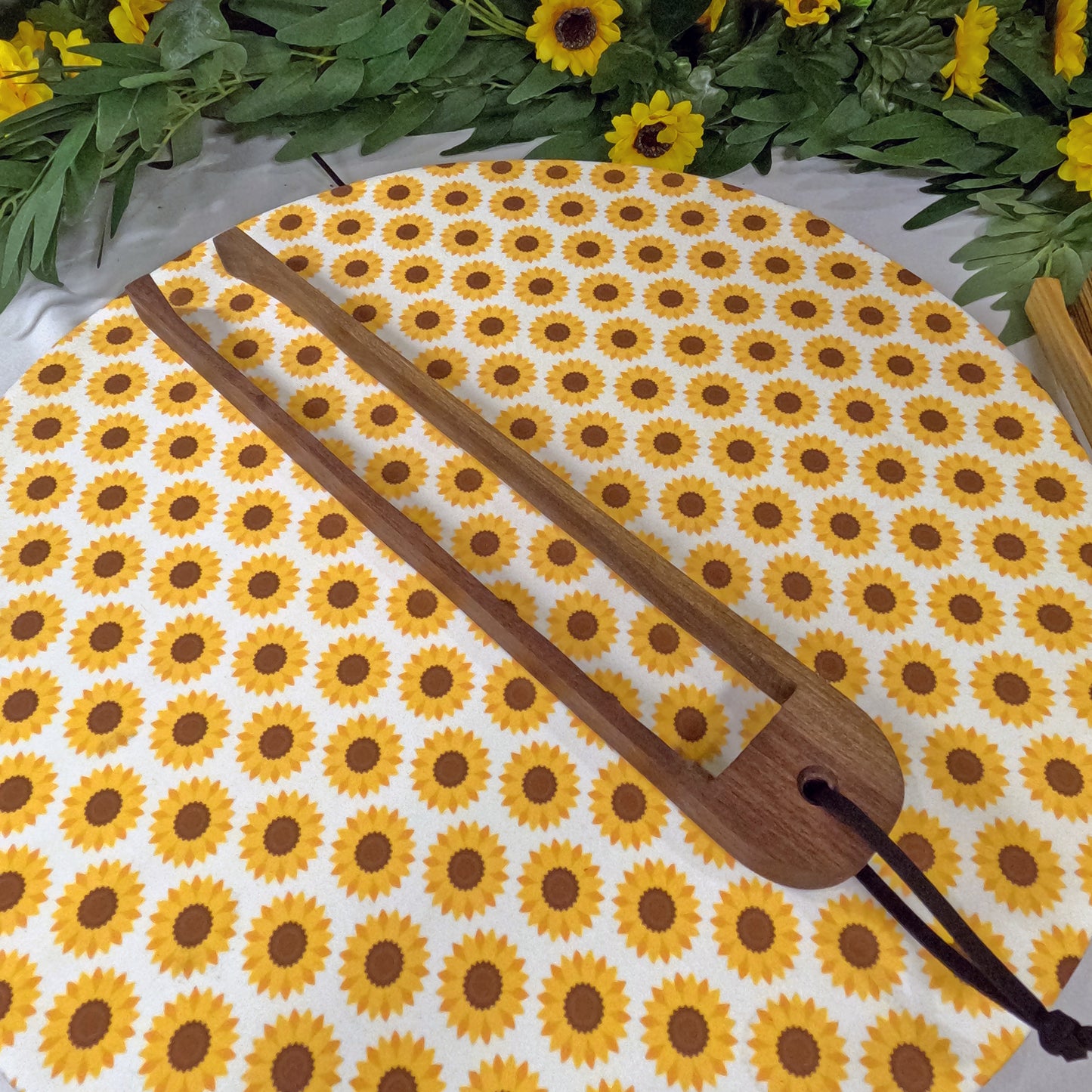 Wooden tongs with sunflower pattern and wooden paddle on a white surface with greenery.