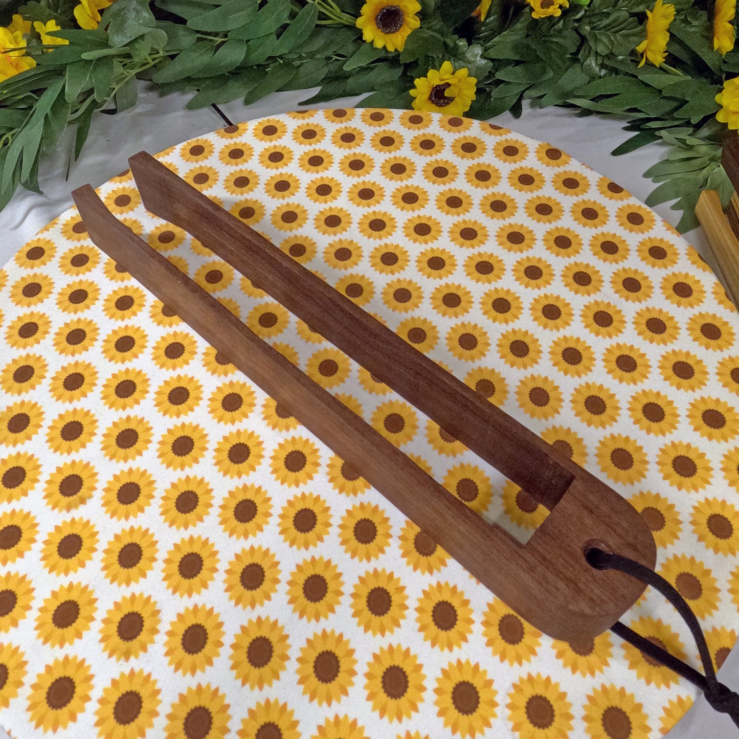 Wooden tongs on a sunflower patterned mat with greenery in the background