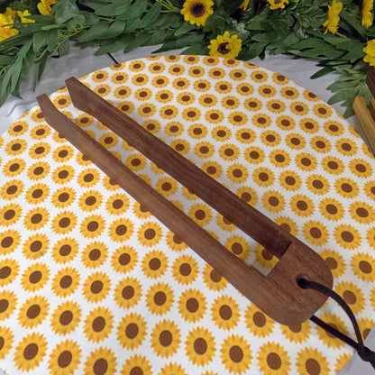 Wooden tongs on a sunflower patterned mat with greenery in the background