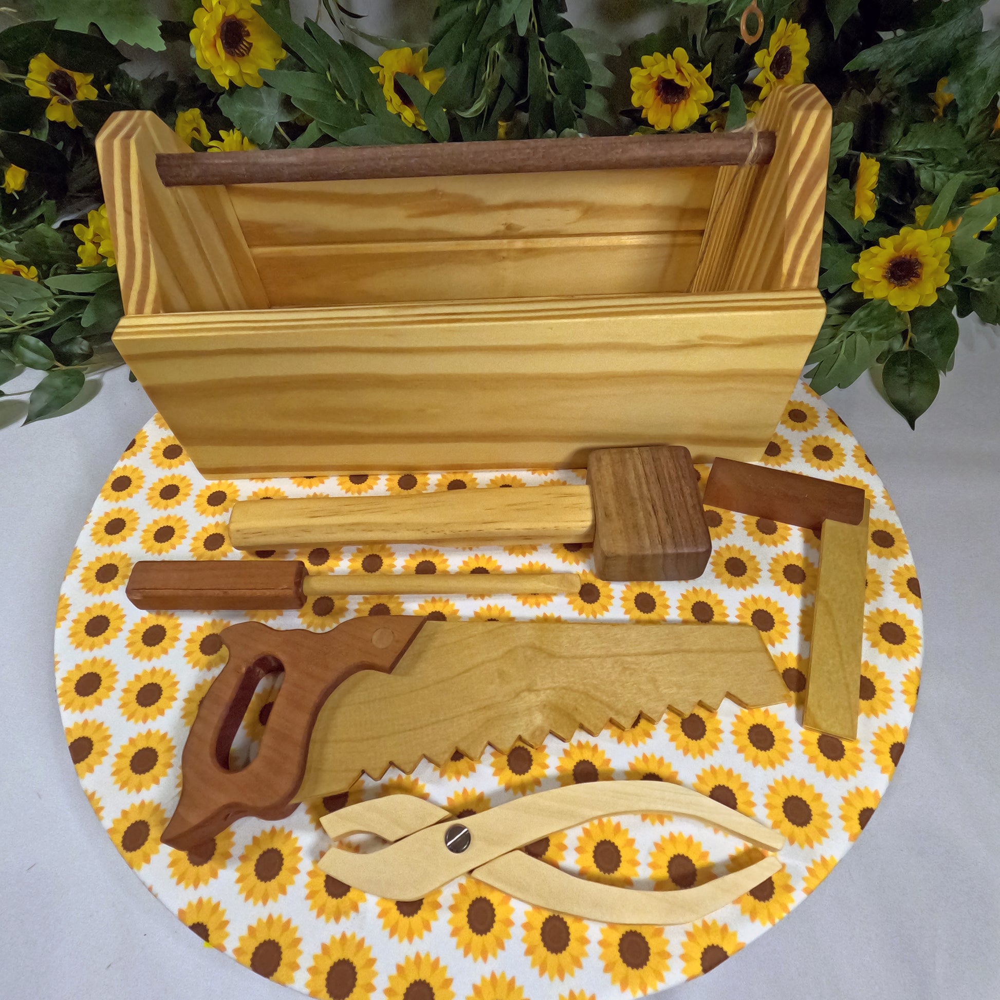 Wooden tool set on a circular mat with sunflower pattern, against a green leafy background.