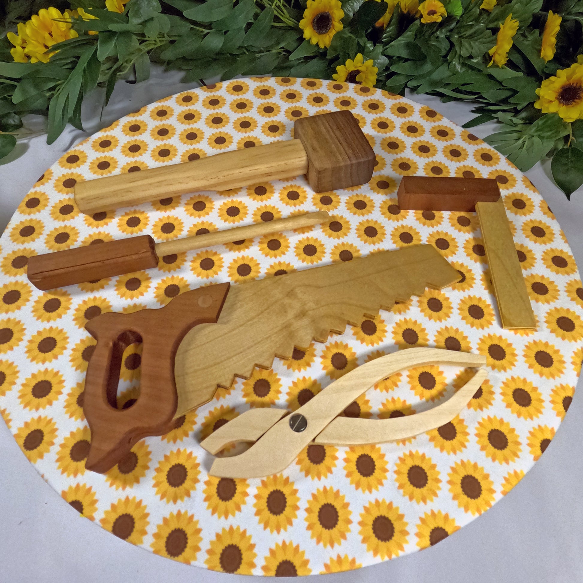 Wooden tools on a round mat with sunflower pattern, surrounded by greenery and flowers.