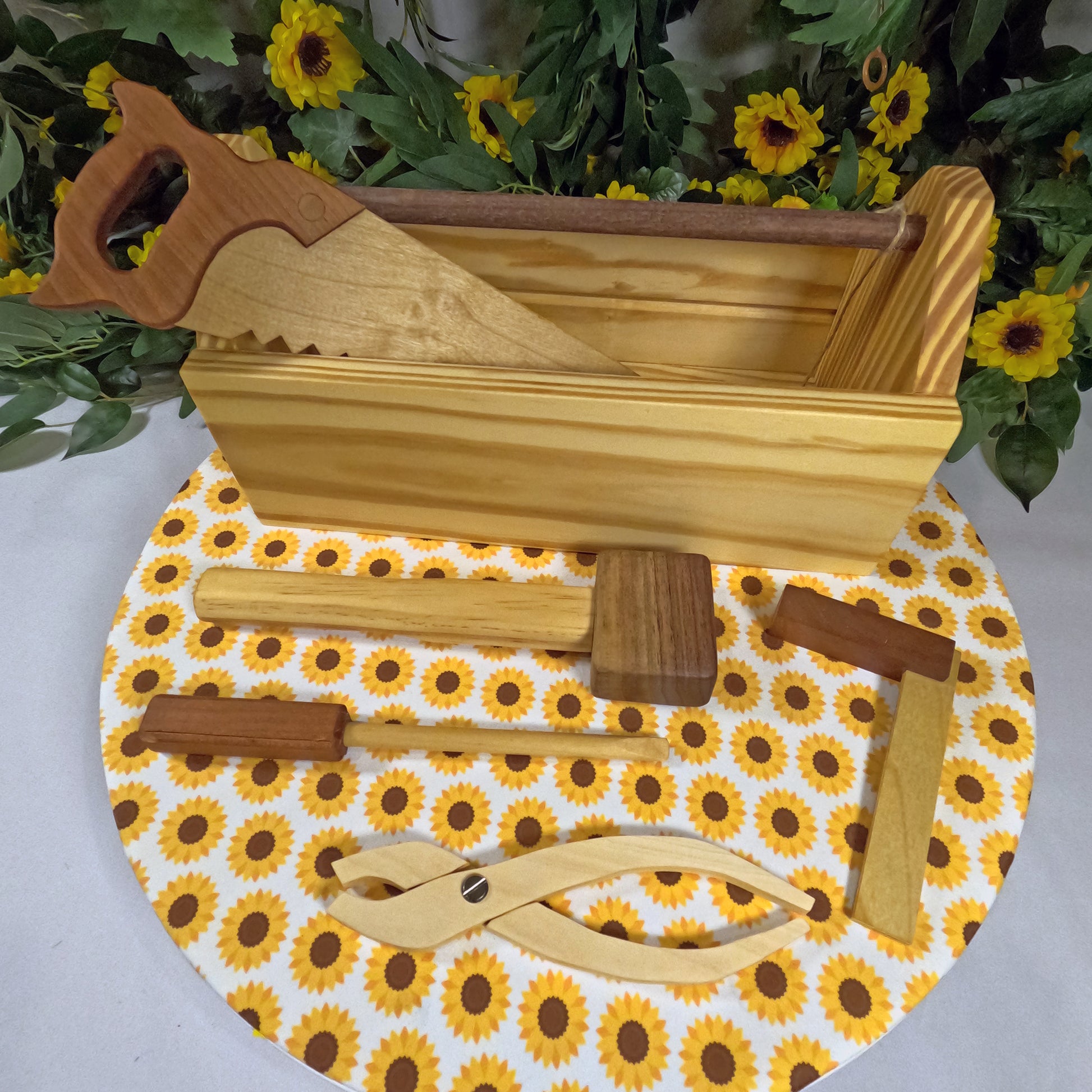 Wooden tools on a round mat with sunflower pattern, surrounded by greenery and flowers.