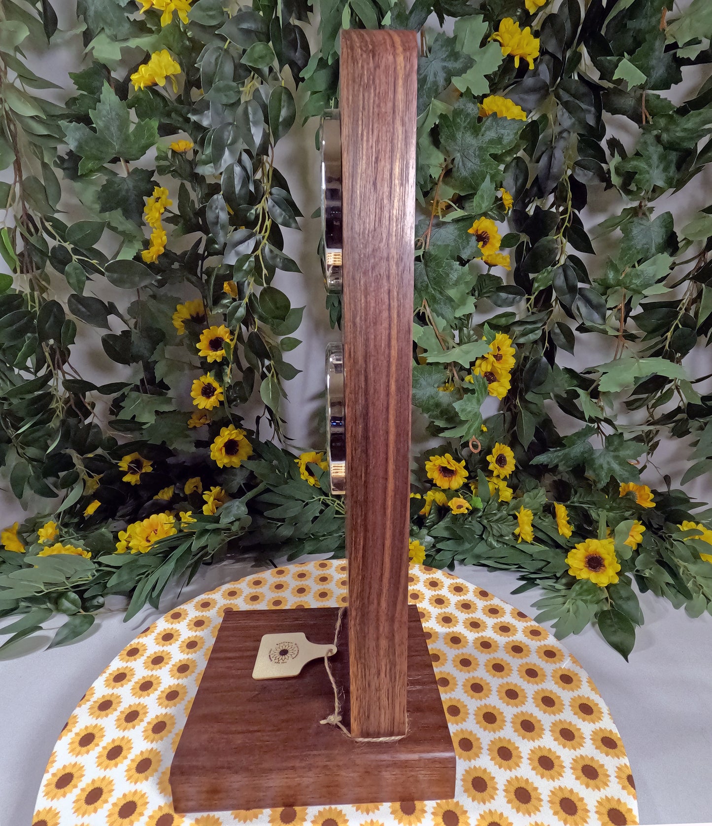 Wooden stand with a decorative tag on a tablecloth with sunflower pattern, against a floral background.
