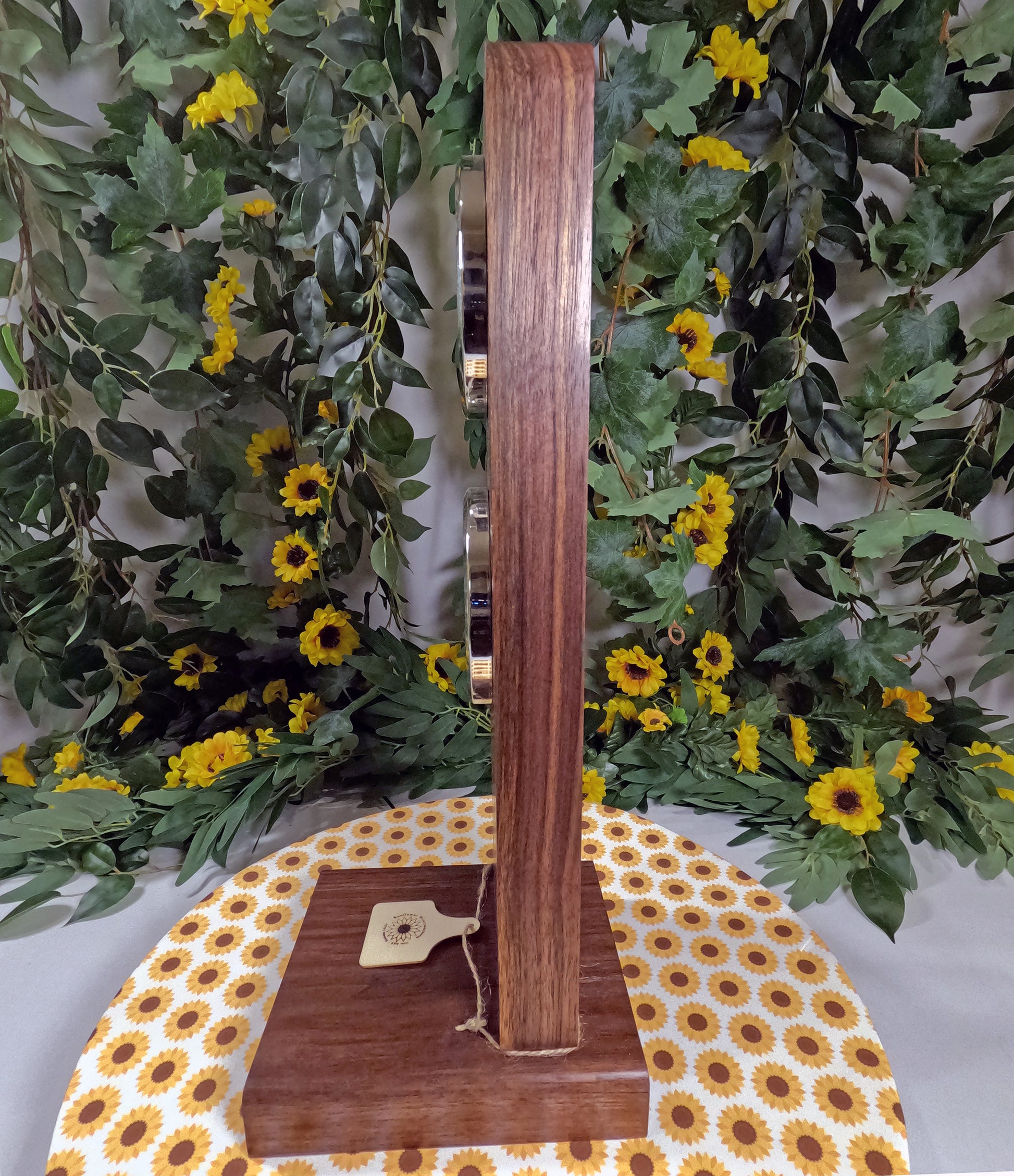 Wooden stand with a decorative tag on a tablecloth with sunflower pattern, against a floral background.