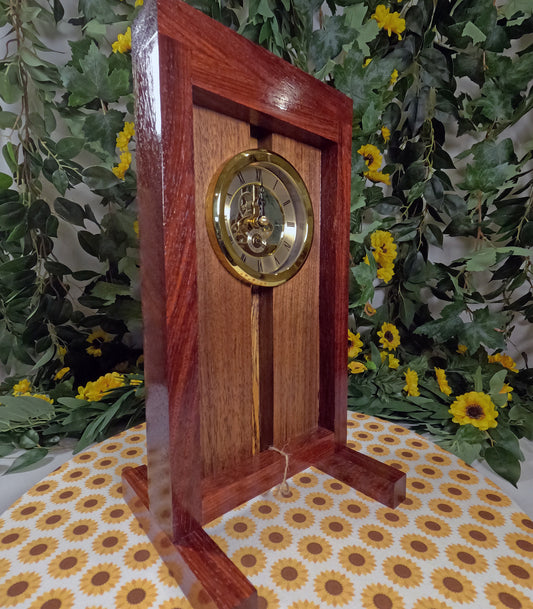 Wooden clock with gold face on a floral-patterned surface with greenery in the background