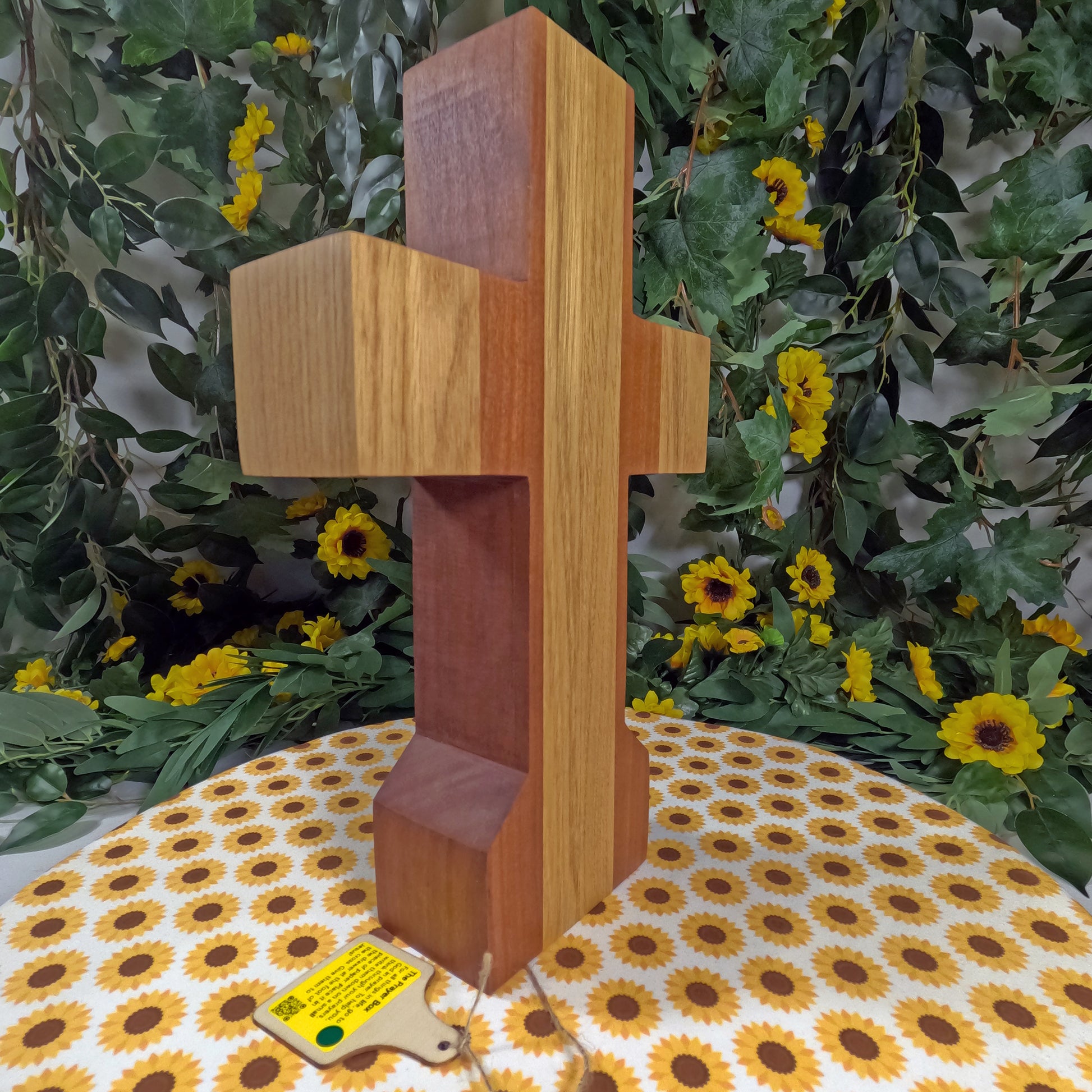 Wooden cross with a yellow label on a floral tablecloth with a green leafy background