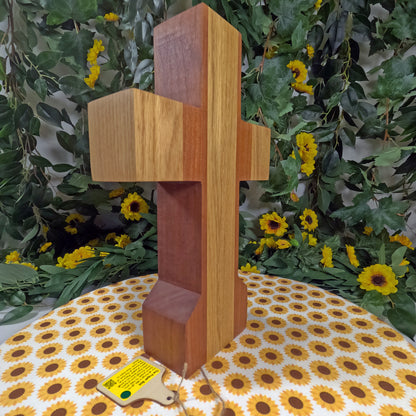 Wooden cross with a yellow label on a floral tablecloth with a green leafy background