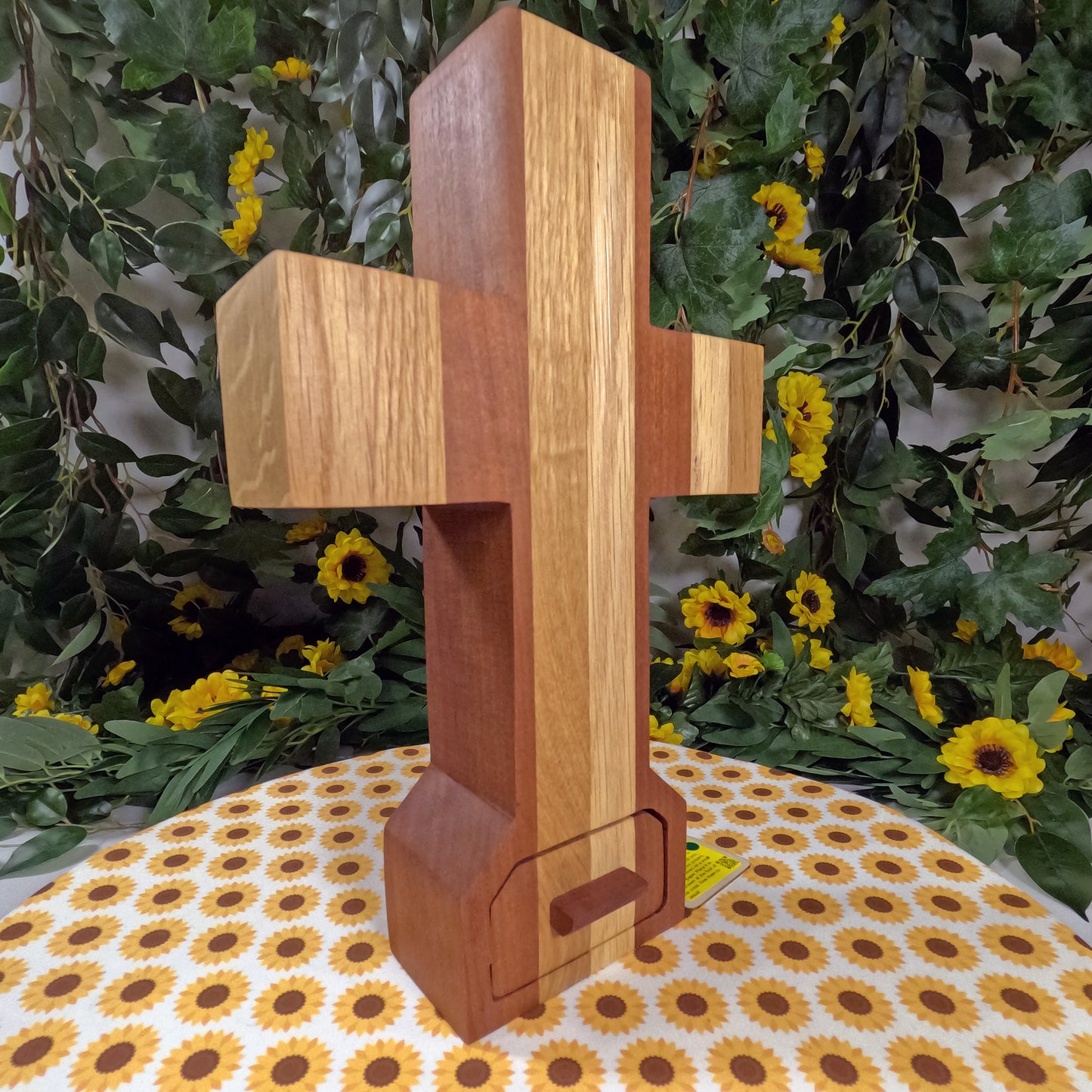 Wooden cross on a floral tablecloth with greenery and flowers in the background