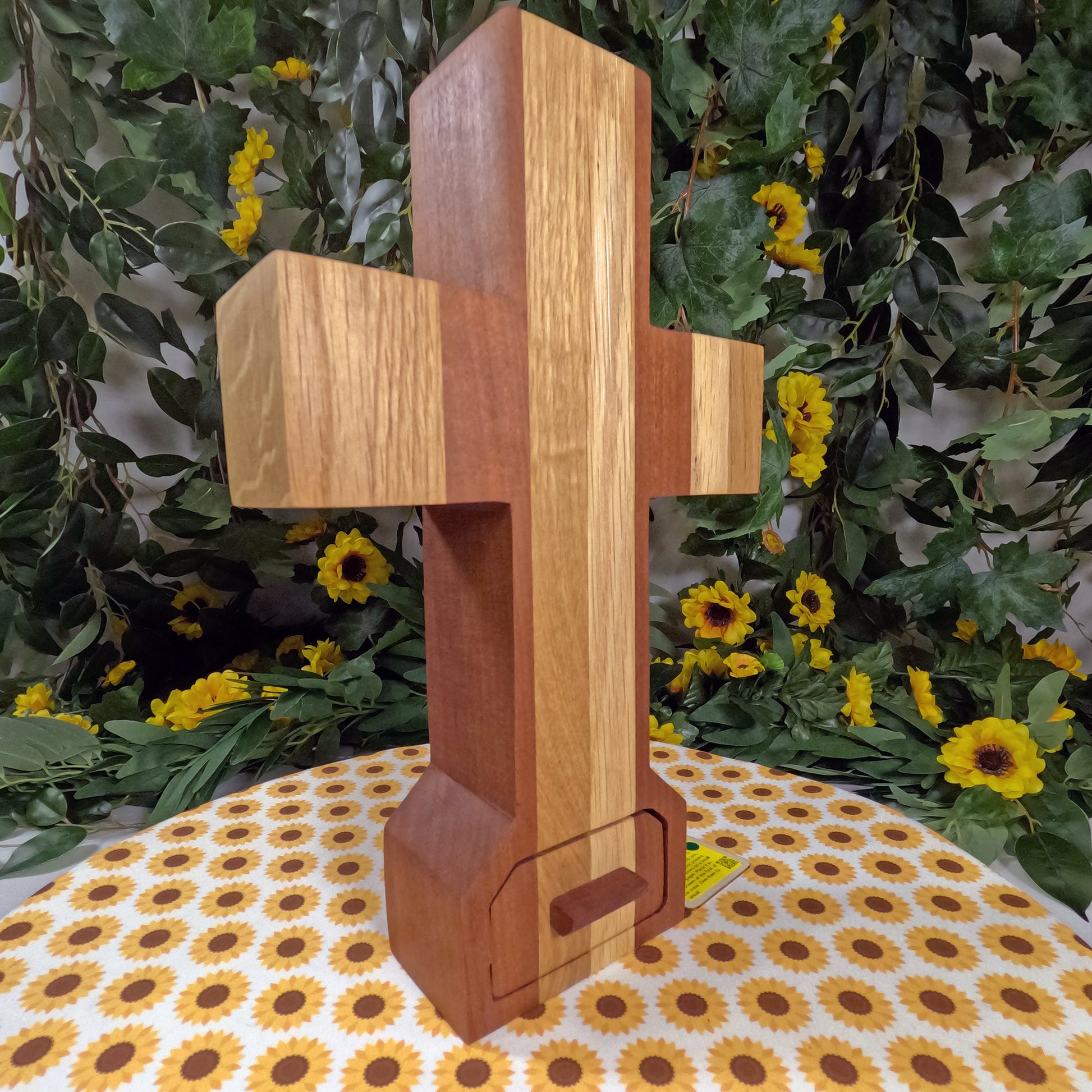 Wooden cross on a floral tablecloth with greenery and flowers in the background