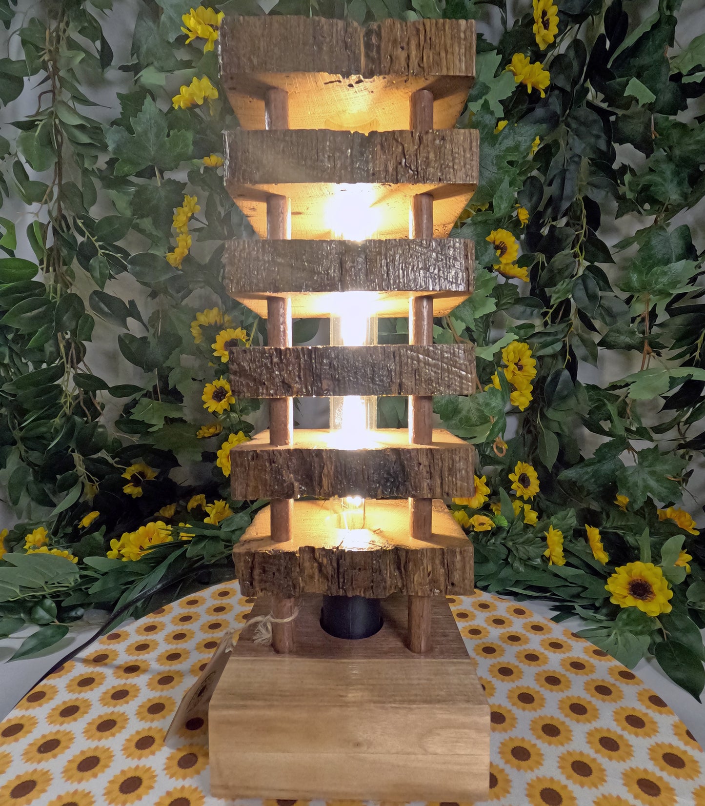 Wooden tiered lamp with warm glow surrounded by greenery and flowers