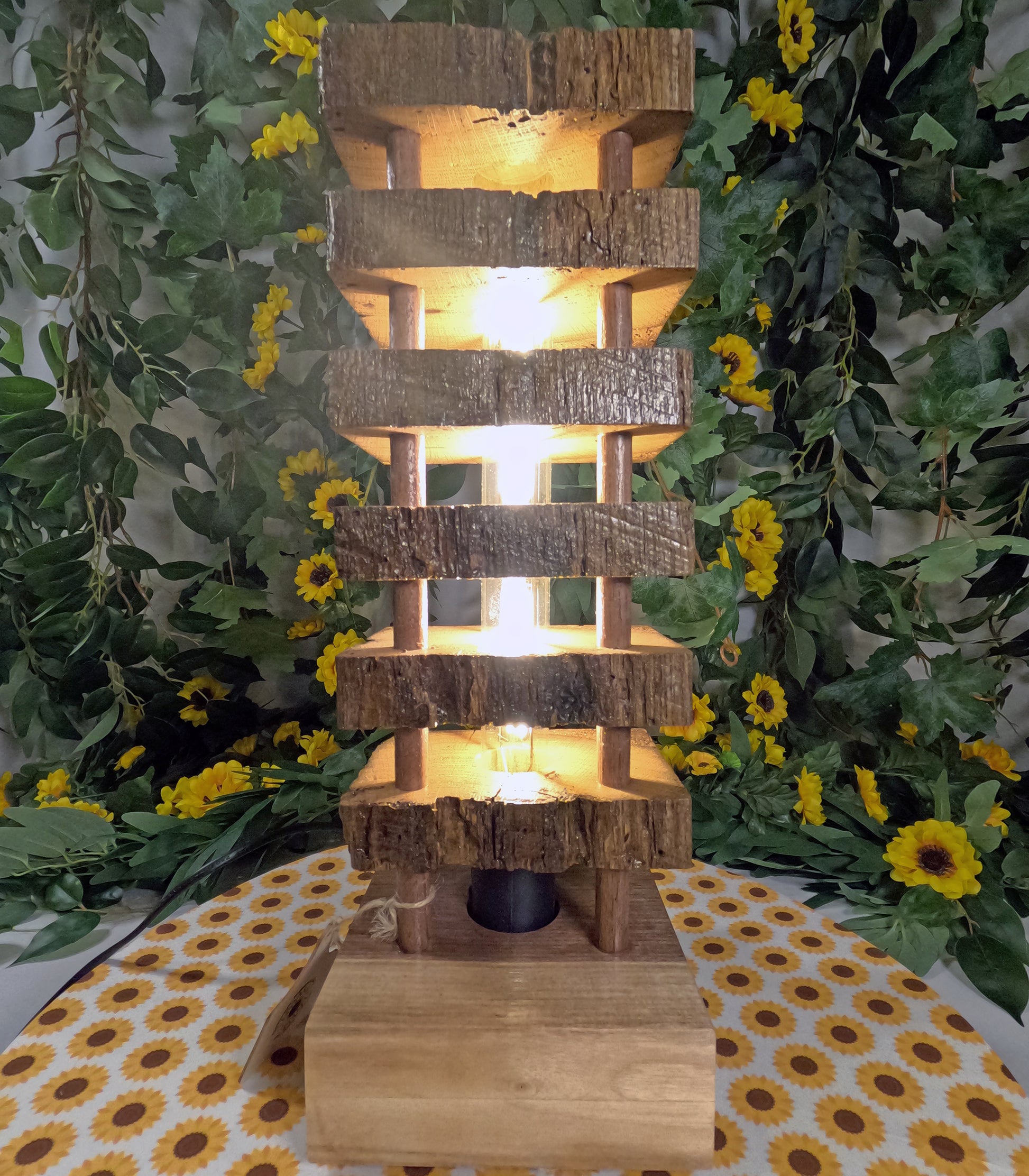 Wooden tiered lamp with warm glow surrounded by greenery and flowers