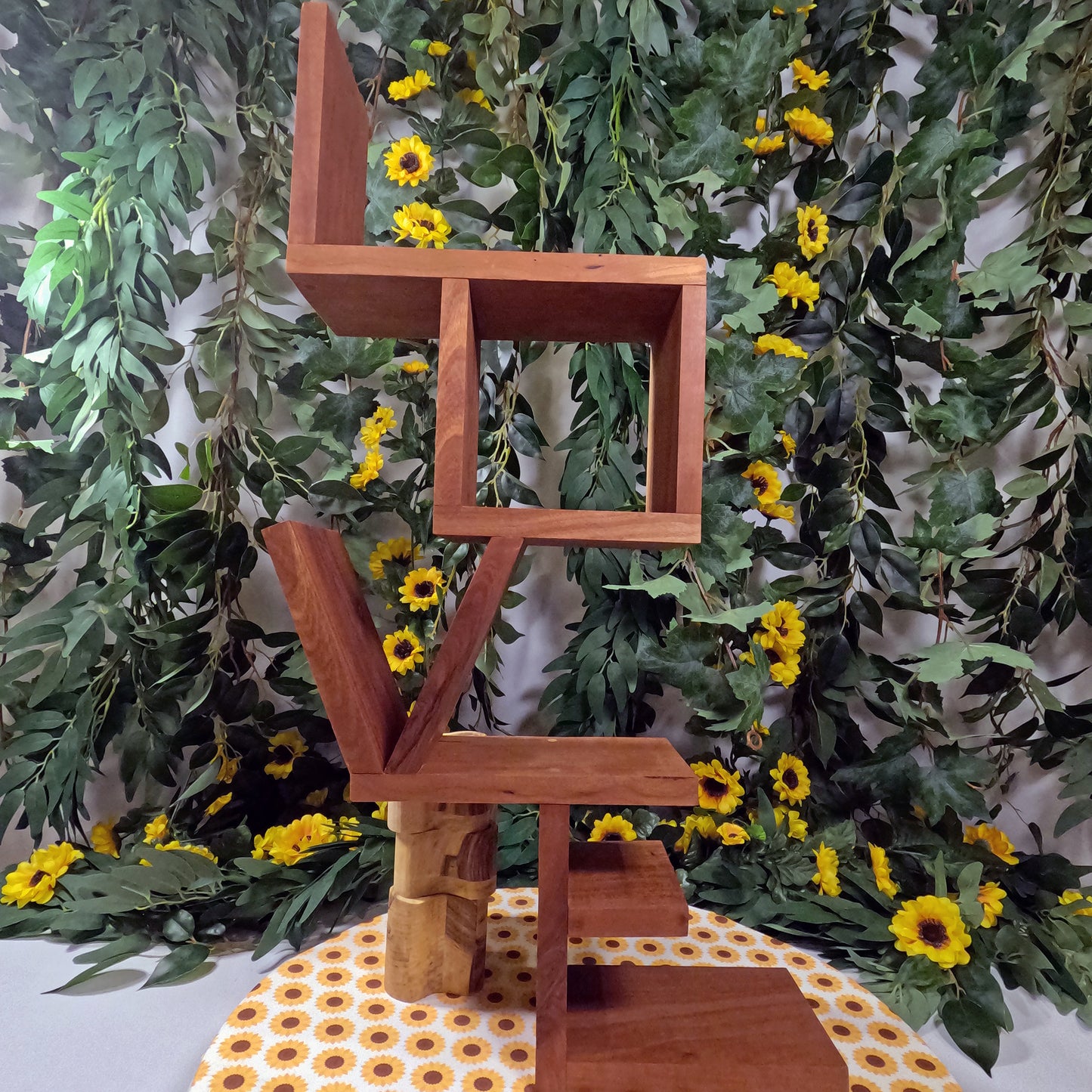 Wooden sculpture with geometric design against a green leafy background